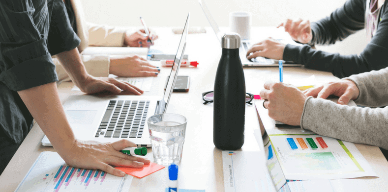 work table with laptops and people writing