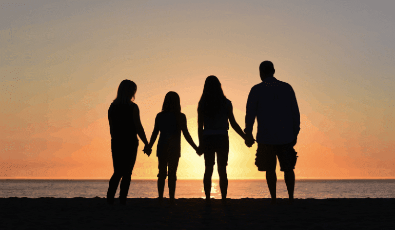 Family in silhouette holding hands at sunset