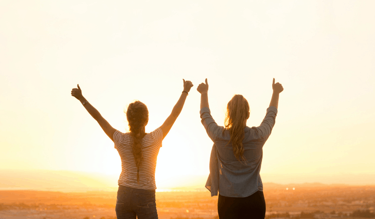 Two women giving thumbs up to the sunrise