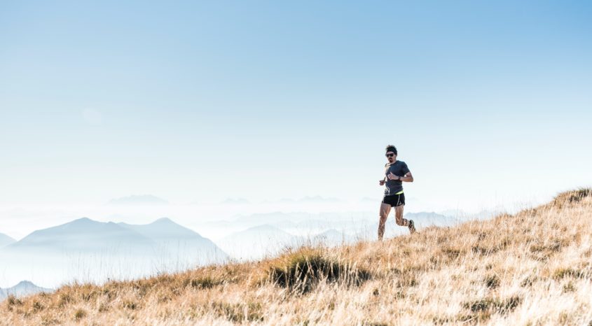Person runs over hill with mountains in background