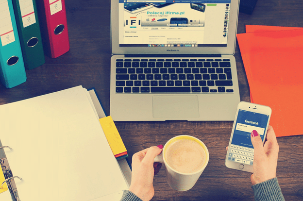 hands holding cup of tea and phone, in front of laptop