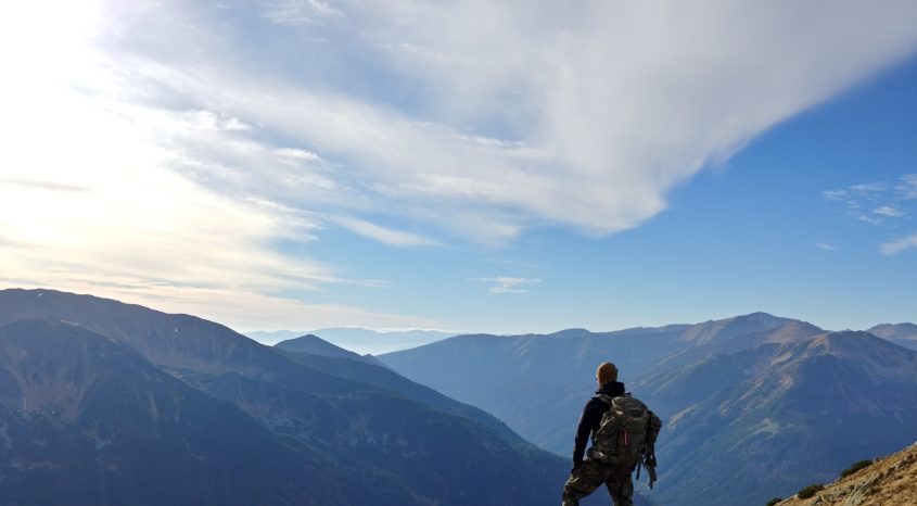 Hiker stands on rocky outcrop looking at mountains in the distance