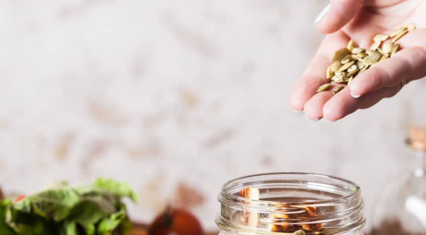 Hand holding seeds with jar and vegetables in background