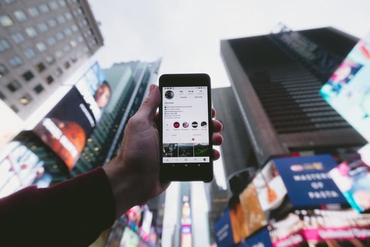 Hand holding mobile phone with tall buildings in background