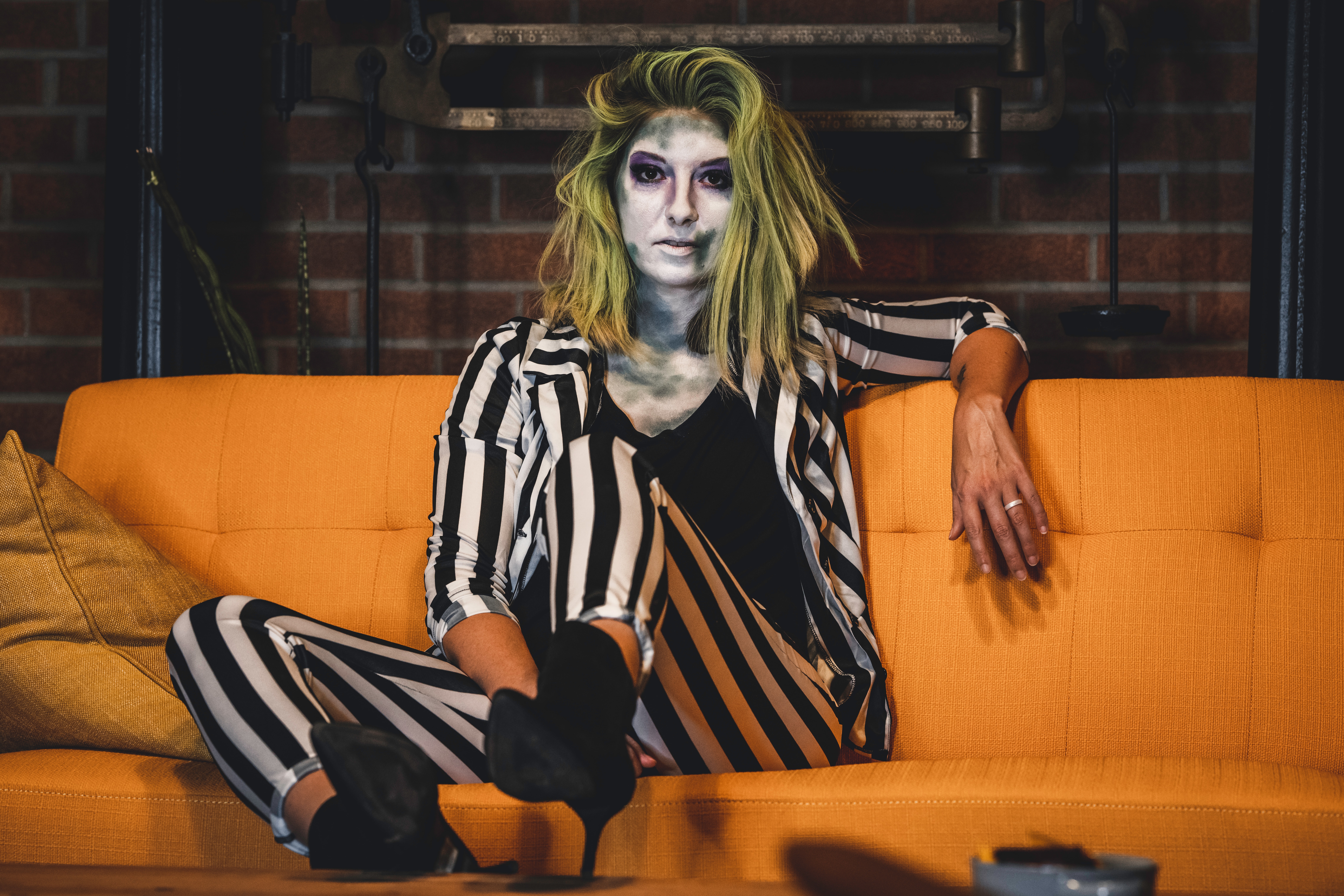 Person dressed in striped suit with halloween style makeup, sitting on orange sofa