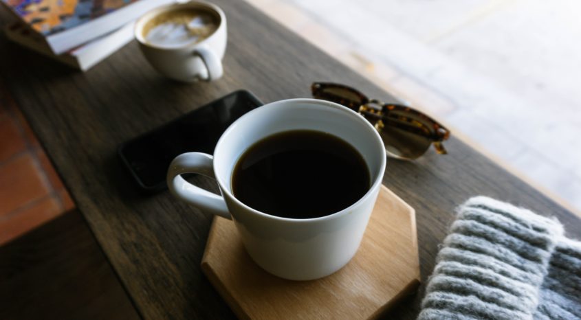 Cup of coffe on table with wooly hat and sunglasses