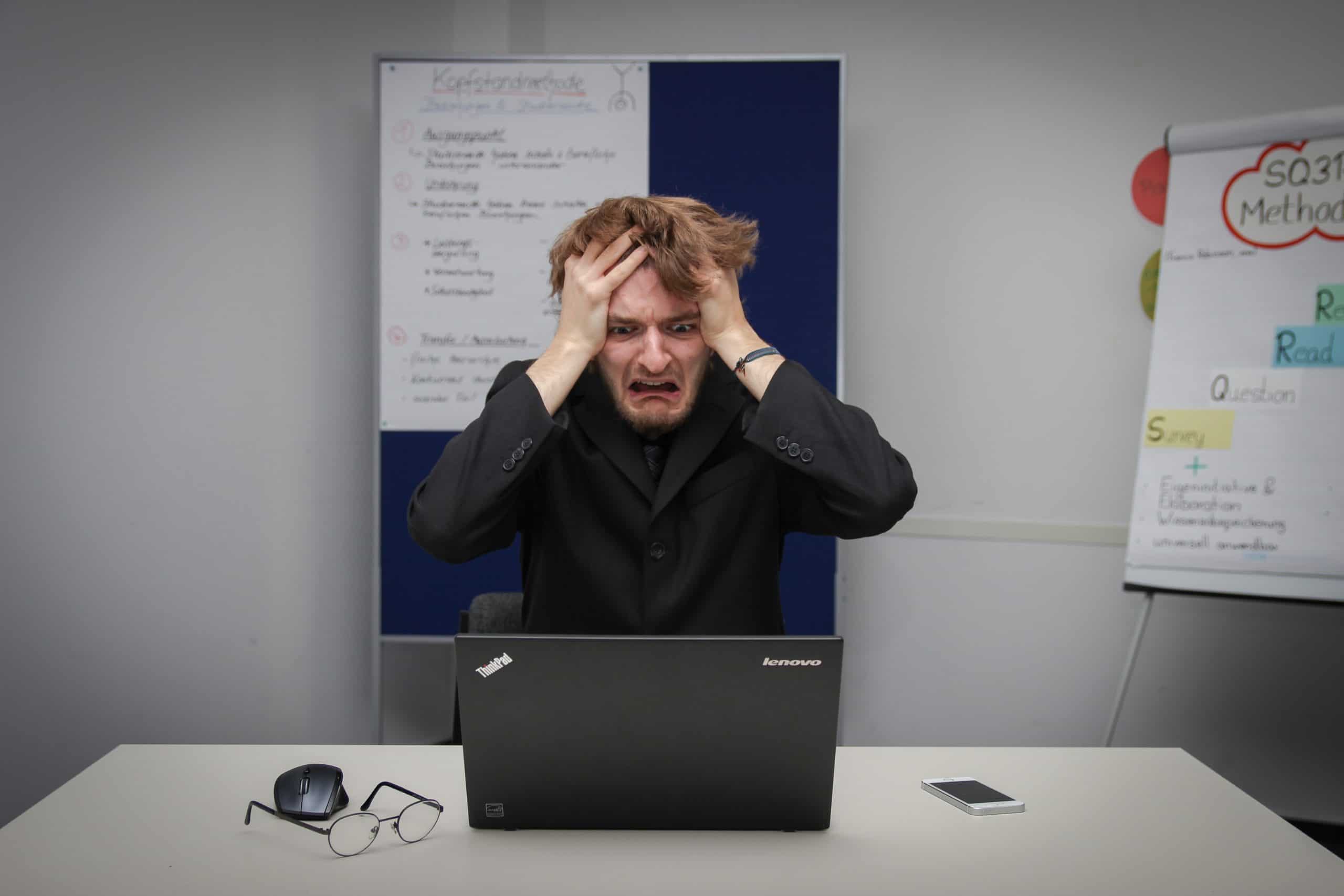 Person holds head whilst staring at laptop