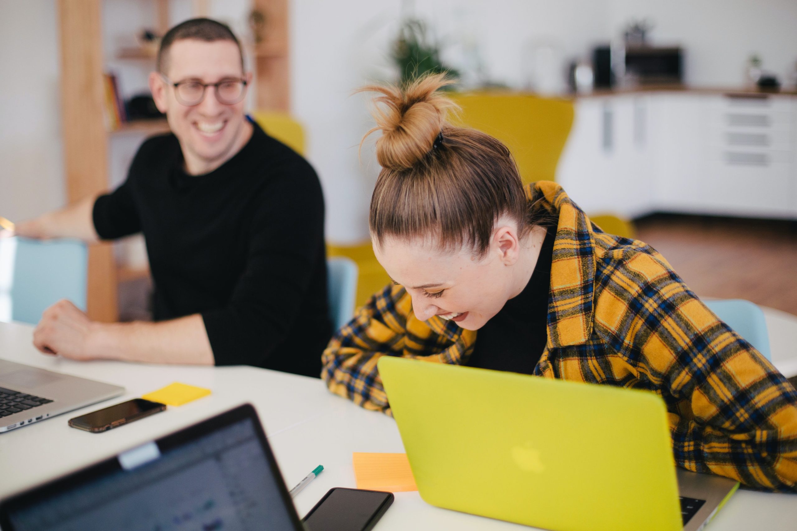 People laughing whilst sitting at office desk with laptops