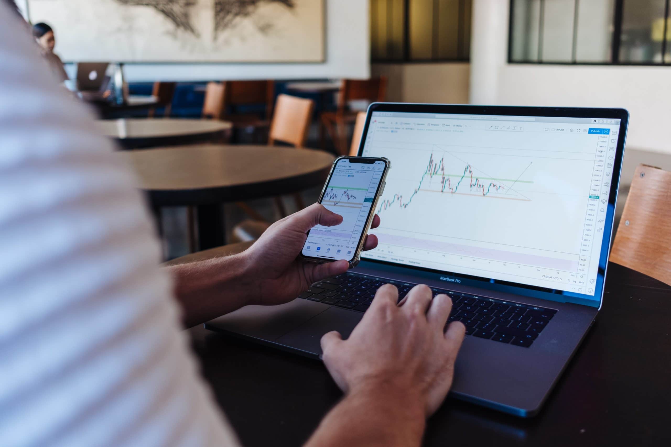 Person holding phone with laptop on table