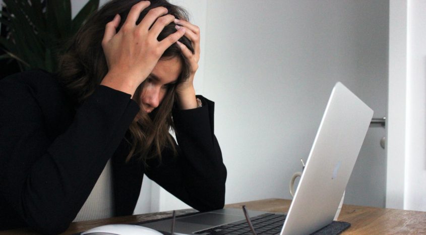 Person sat in front of laptop holding head in hands