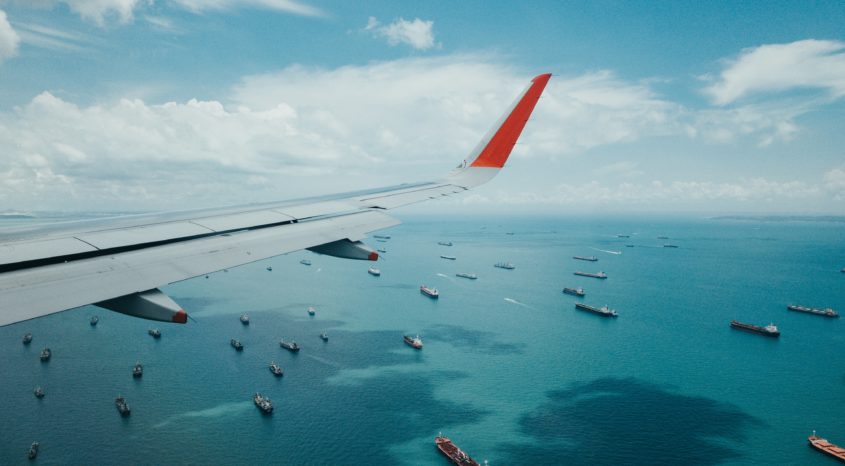 airplane wing with container ships on ocean below
