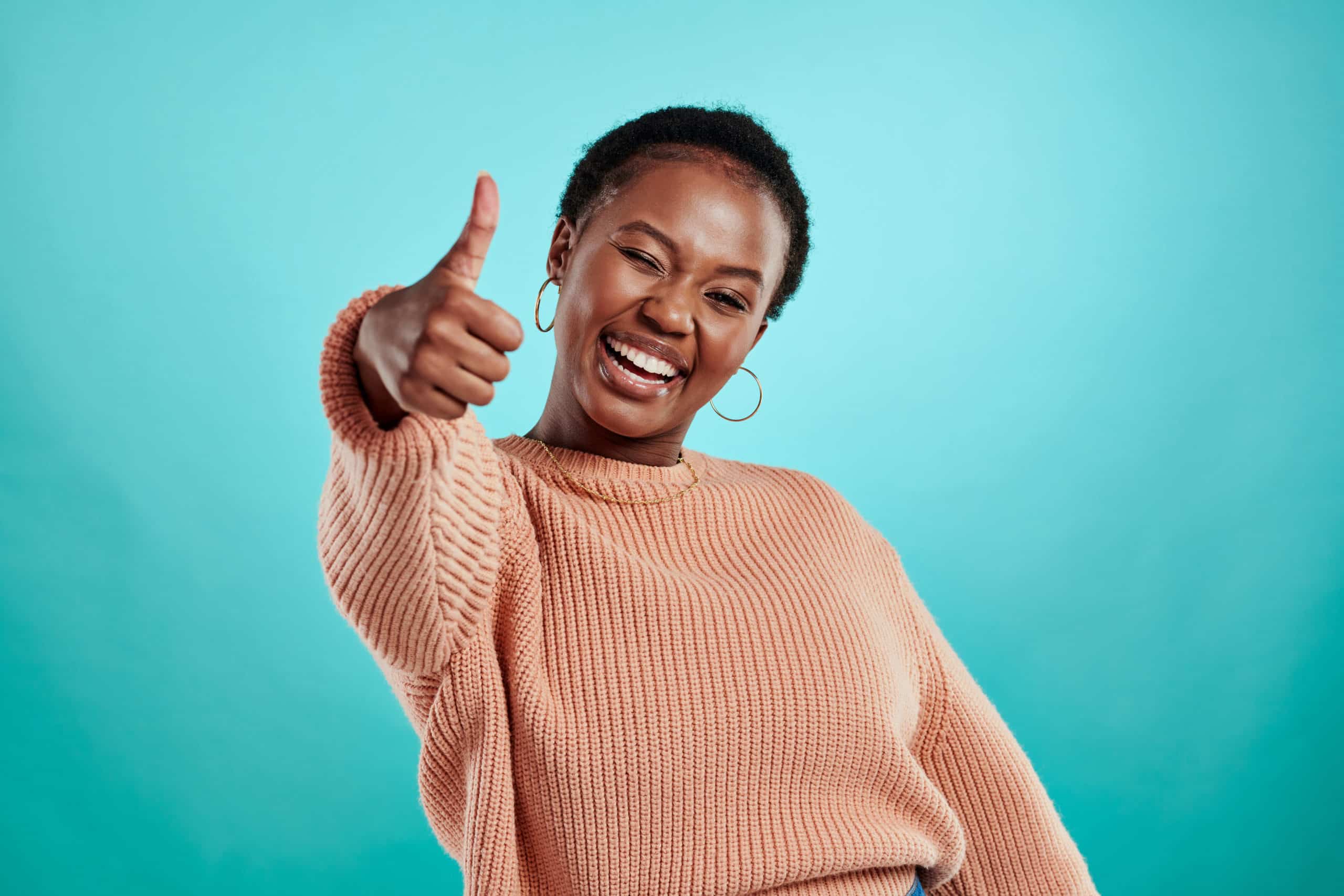 Person showing thumbs up while standing against a turquoise background