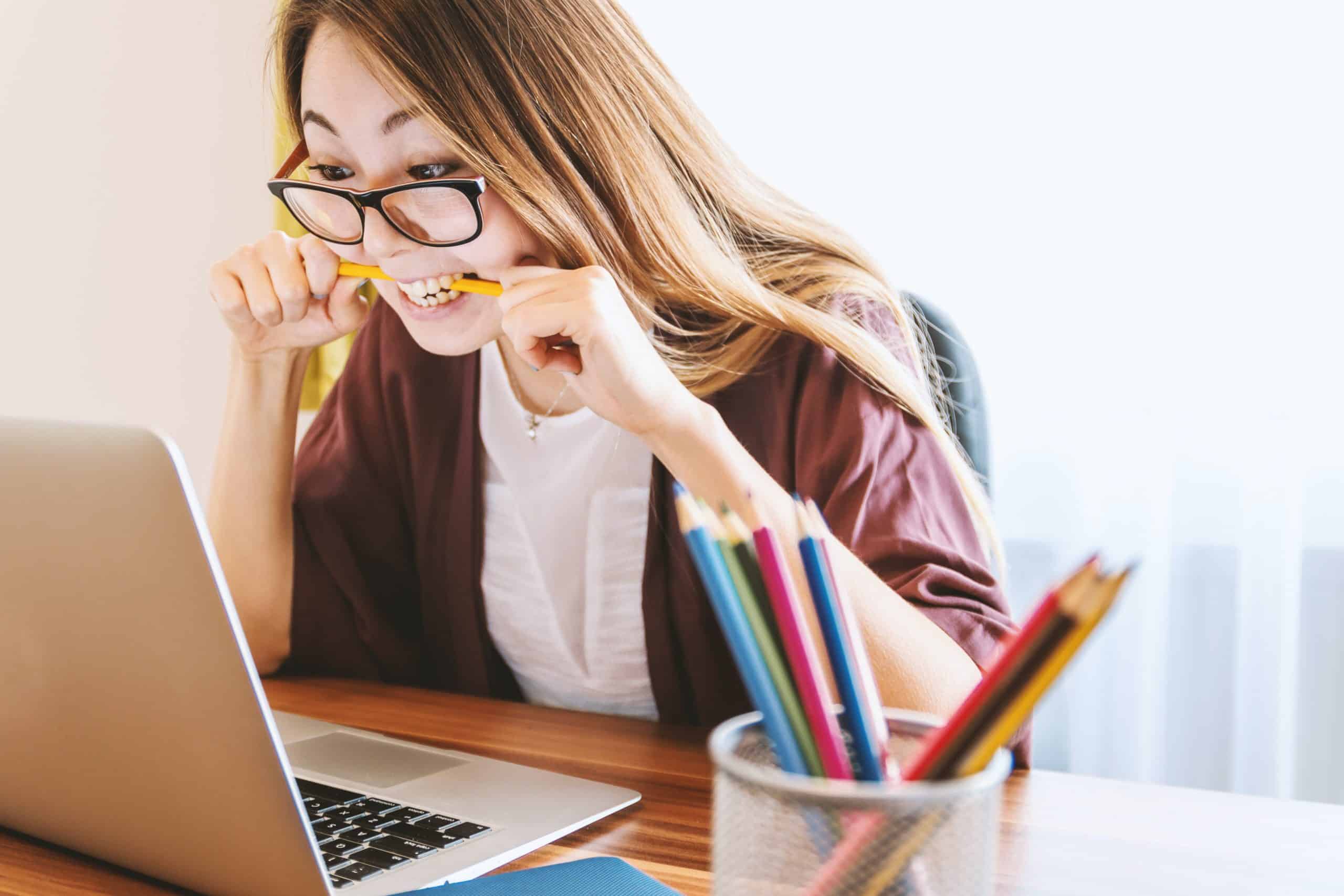 Person sat in front of laptop biting pencil in frustration