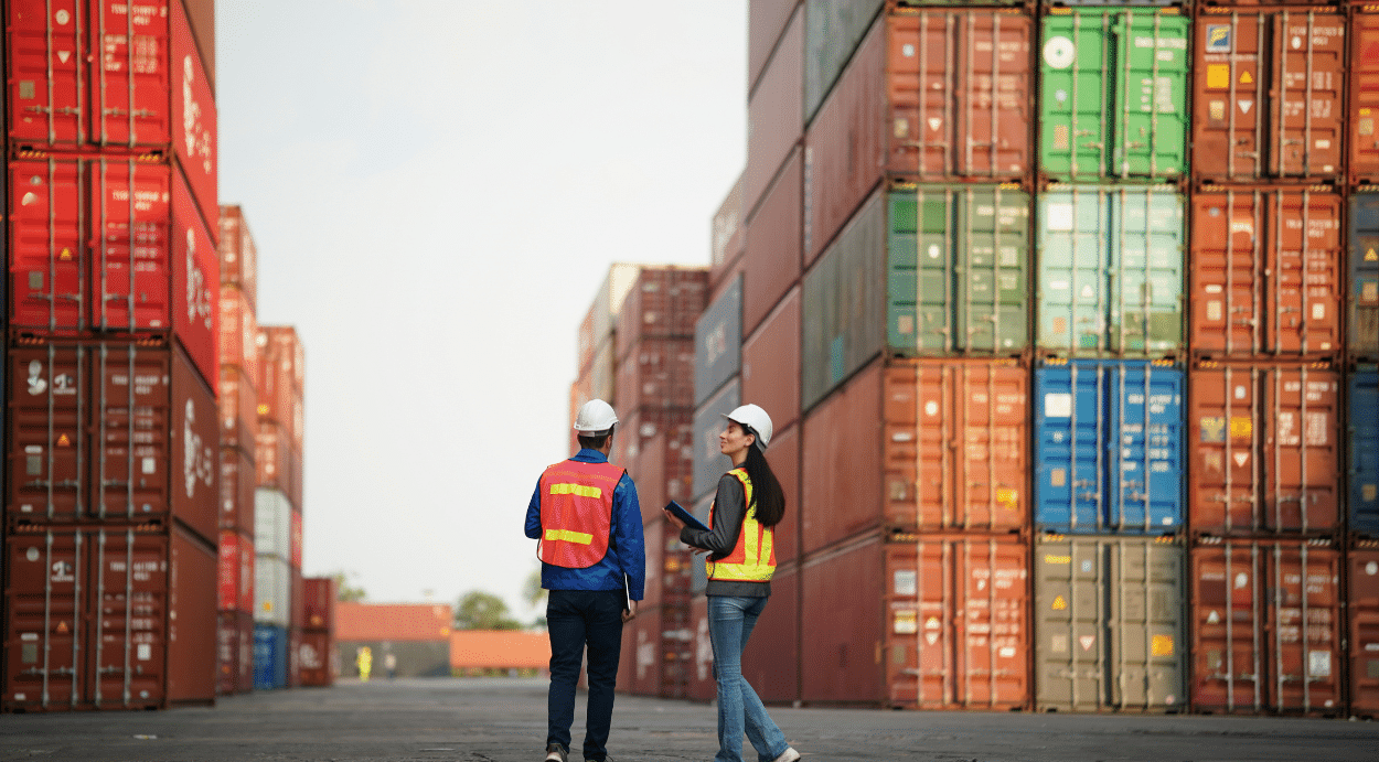2 Workers walking in front of a pile of containers.