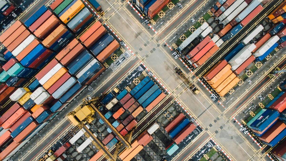 Top-down view of stacked shipping containers at a port terminal, representing supply chain operations and freight movement.