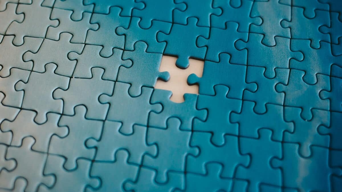 Near-complete blue jigsaw puzzle with a single central piece missing, revealing a bright light underneath.